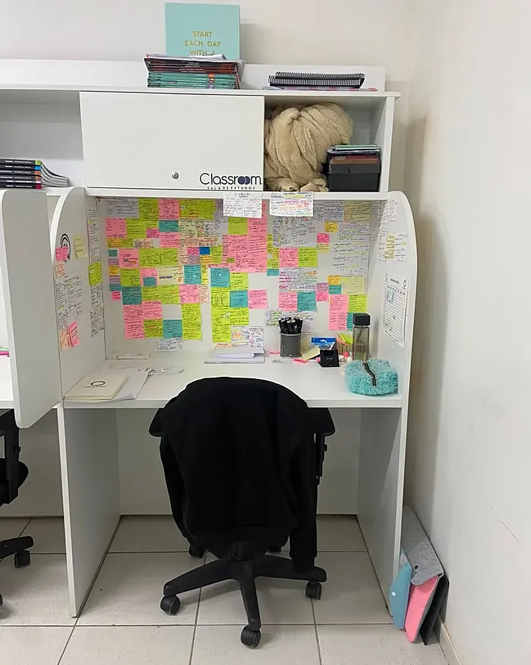 Bancada individual com material de estudo organizado e lembretes na parede