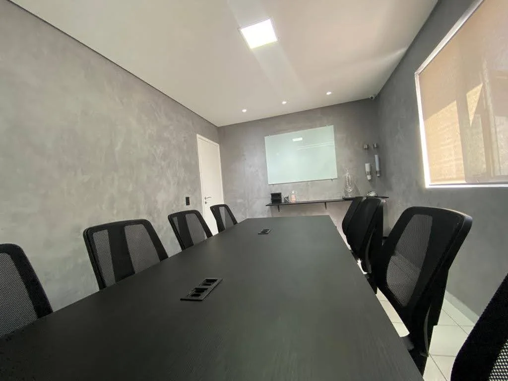 Sala de reunião da Classroom Graças vista da mesa, com o quadro de vidro ao fundo e tomadas na própria mesa